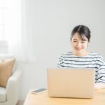在宅勤務でノートパソコンを使って働く女性。自宅の明るい書斎で集中して仕事をする様子