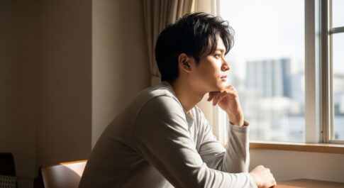 自室の窓際席で少し考え込んでいる男性