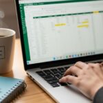 ノートパソコンの画面にExcelの表が映し出されており、そのキーボードをタイピングする手元のクローズアップ写真